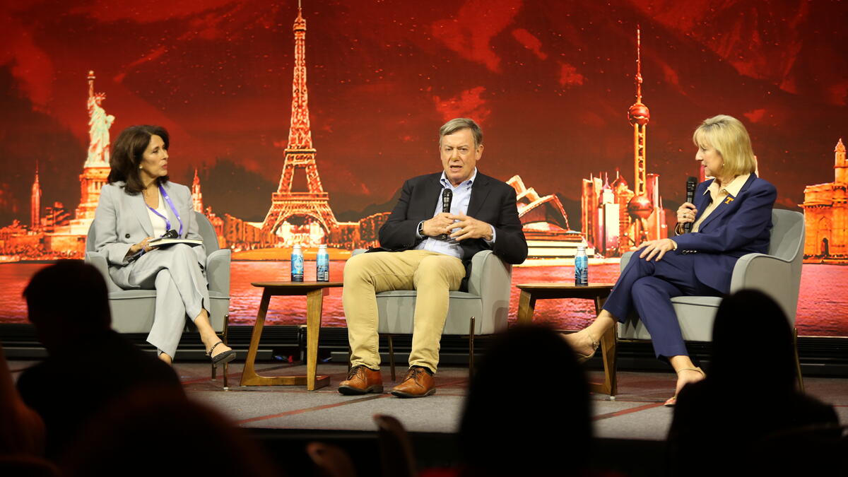 Three people sit on on-stage discussing the need for collaboration in higher education.