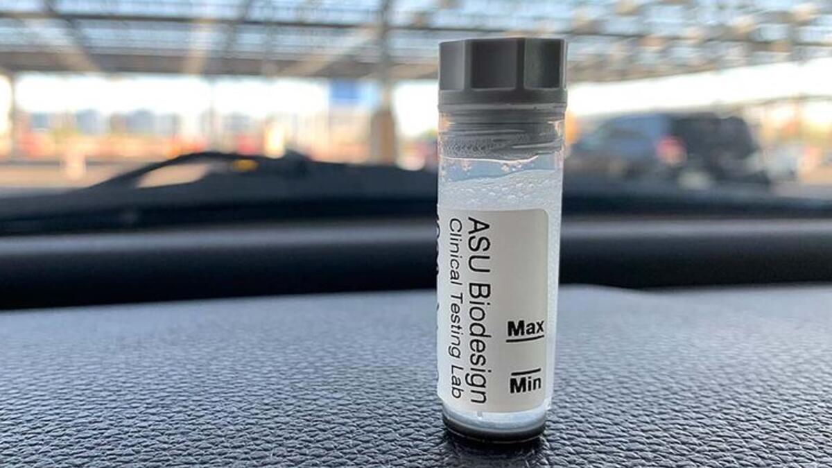 A COVID-19 saliva test vial from ASU Biodesign sits on a car dashboard