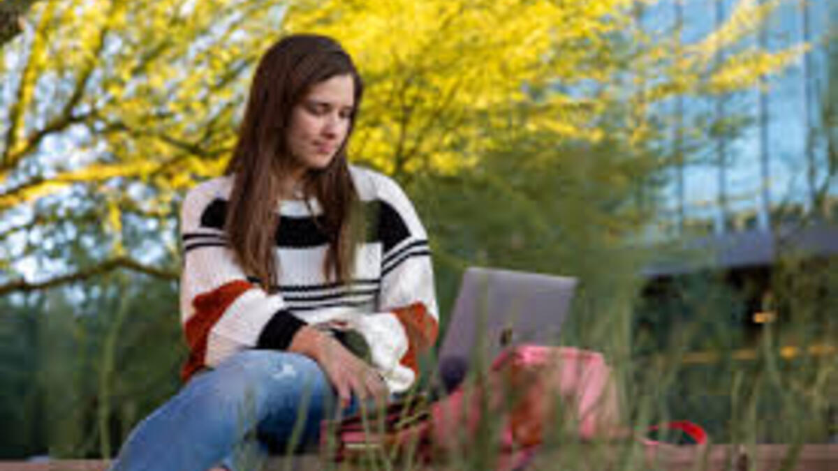 A student sits outside a building working on a laptop.