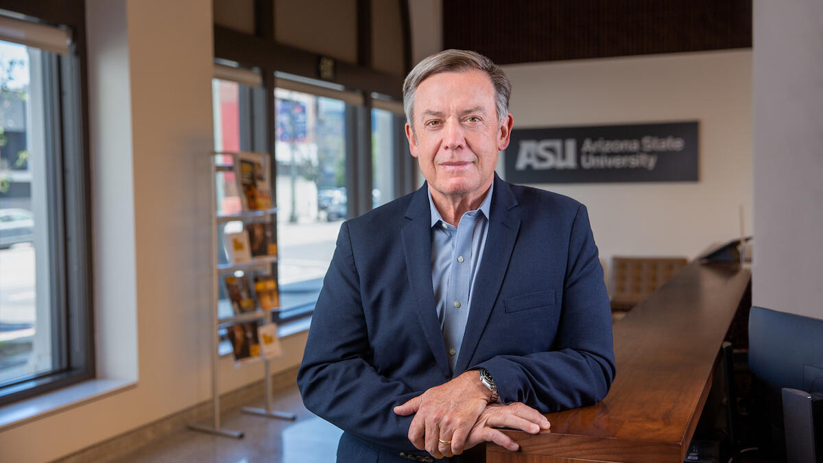 A person wearing a blue jacket and shirt leans on a wooden reception desk in the lobby of the ASU California Center.