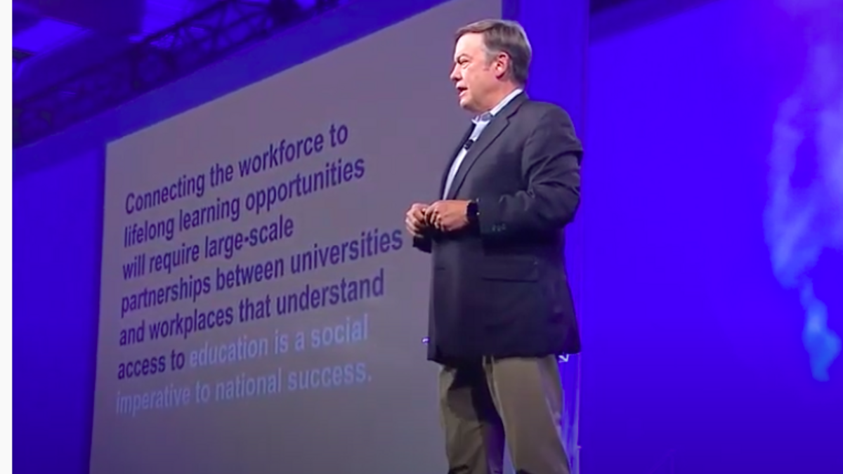 A middle-aged man in beige slacks and a blue jackets stands on a stage in front of a PowerPoint slide at the 2019 ASU GSV Summit.